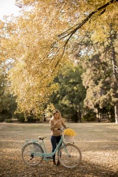 Pretty young woman with bicycle using smartphone in autumn park