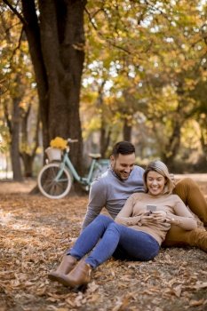 Young couple sitting on ground and using mobile phone in autumn park