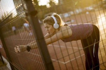 Pretty young woman with earphones stretching during sport training