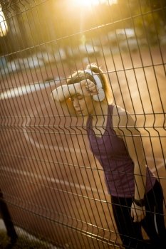 Sporty young woman resting by metal fence on court