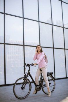 Young woman with ebicycle using on mobile phone outdoor