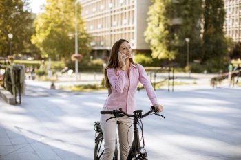 Young woman riding an electric bicycle and using mobile phone in urban environment