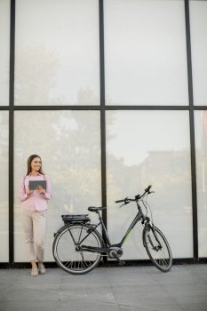 Young woman with tablet and e-bike outdoor on sunny day