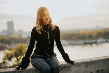 Portrait of trendy young woman listening music from smartphone outdoor at sunset