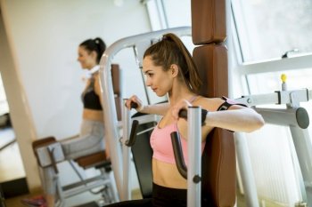 Pretty young determined fitness woman doing exercises at chest press machine at modern gym