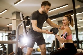 Attractive woman and a personal trainer with dumbbell weight training at the gym