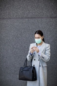 Pretty young woman with protective facial mask on the street using mobile phone