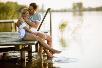 Loving couple sitting on the pier on lake at summer sunset