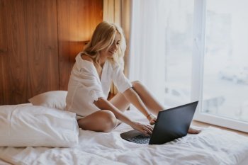 Portrait of a smiling casual young woman using laptop in bed at home