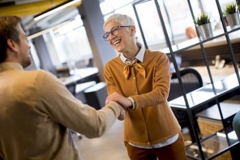 Grateful senior  businesswoman  boss lady hold hand of best employee,  shake hands warm welcoming standing in coworking space