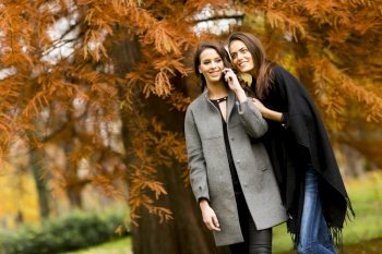 Two pretty young women using mobile phone in the autumn forest
