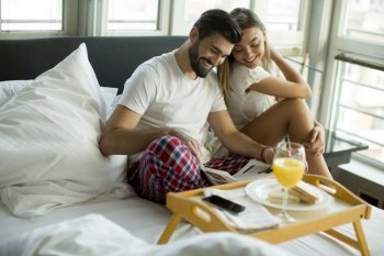 Happy young smiling couple having romantic breakfast in bed in the morning