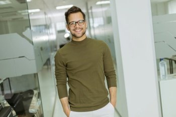 Handsome smiling young businessman in glasses standing in the modern office