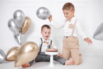 Two boys celebrating birthday, children have a B-day party. Birthday cake with candles and balloons. Happy kids, celebration, white minimalist interior. Two boys celebrating birthday, children have a B-day party. Birthday cake with candles and balloons. Happy kids, celebration, white minimalist interior.