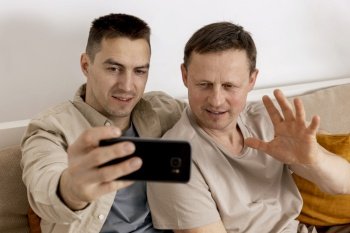 Happy gay couple with casual clothes holding smartphone and talking with friends online, having video call. Homosexual relationships and alternative love. Happy gay couple with casual clothes holding smartphone and talking with friends online, having video call. Homosexual relationships and alternative love.