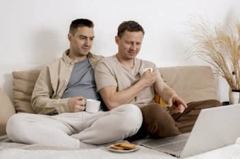 Happy gay couple with casual clothes spending time together at home, watching movie on the laptop and drinking tea. Two caucasian men relaxing. Homosexual relationships and alternative love. Happy gay couple with casual clothes spending time together at home, watching movie on the laptop and drinking tea. Two caucasian men relaxing. Homosexual relationships and alternative love.
