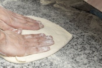Chef’s hands kneading a pizza on gray granite countertop
