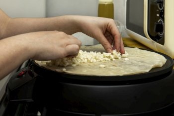 Female chef hands placing grated cheese on top of a pancake being cooked on a round electric plate
