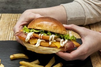 Hands firmly holding a crispy chicken burger with freshly cut tomatoes, fresh lettuce and mayonnaise