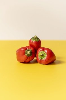 Front image of three red peppers on yellow table and white background.