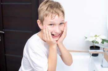 The boy holds his wet hands to his face for washing. Cute boy washes and laughs