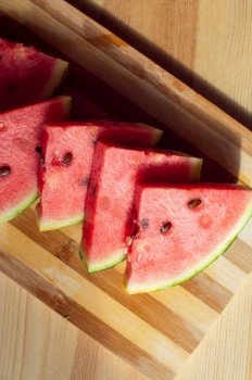 A ripe watermelon cut into slices lies on a wooden table. A sliced ripe watermelon is lying on a wooden table