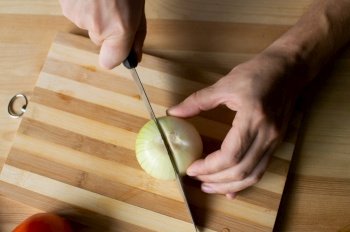Men’s hands cut onions with gozh on a wooden board. Men’s hands cut onions on a wooden board