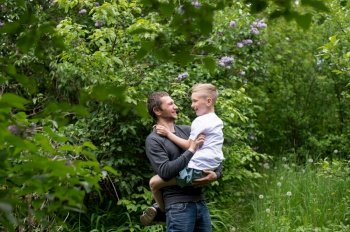 holding a child in your arms, sitting in your arms, studying, dad, son, child, father, parenting, interest development, watching, playing, family vacation, nature walk, spring, flowering tree. The boy is sitting in Dad’s arms and they are laughing