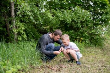 Dad next to his son, sitting next to him, white T-shirt, daddy’s son, walking on the street, looking for bugs, biology. The boy is sitting next to his dad, looking at the ground