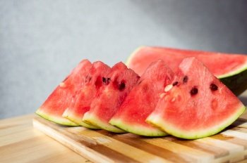 A ripe watermelon cut into slices lies on a wooden table. A sliced ripe watermelon is lying on a wooden table