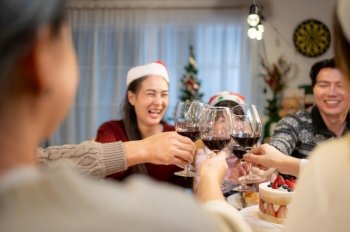 Happy asian family celebrating Christmas together at home. Cheerful senior parents and children in Santa hat clinking glasses of red wine.