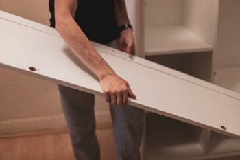Young caucasian man holding side part of wardrobe in bedroom, side view closeup with selective focus. Furniture assembly concept.. A young man holds the side door of a wardrobe.