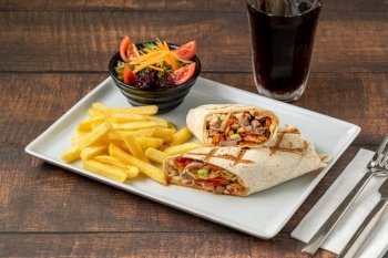 Meat wrap cut in half with french fries on dark stone table