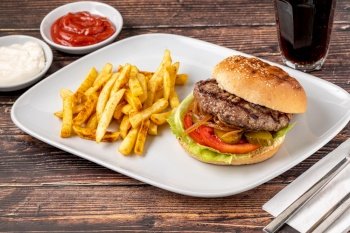 Delicious grilled burger on white plate on wooden table. With sauces and french fries