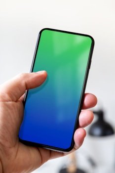 Hand holding a smartphone with blank blue and green screen. White office background.. Hand holding a smartphone with blank blue and green screen. Office background.