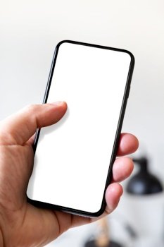 Hand holding a smartphone with blank white screen. White office background.. Hand holding a smartphone with blank white screen. Office background.