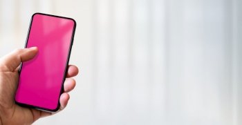 Hand holding a smartphone with blank pink screen. White office background. Horizontal banner.. Hand holding a smartphone with blank pink screen. Office background. Horizontal banner.