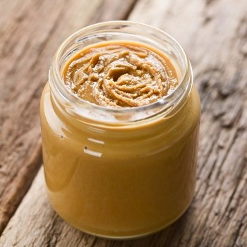 Creamy smooth peanut butter in jar, photographed on wood (Selective Focus, Focus in the middle of the peanut butter). Creamy Smooth Peanut Butter in Jar