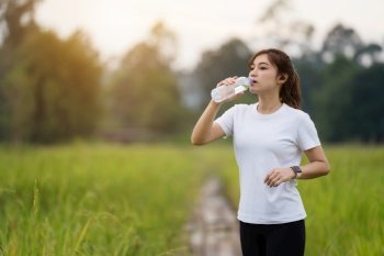 sporty woman drinking water after running in the field