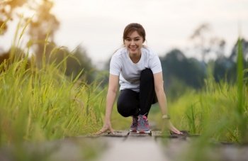 young woman in starting position ready for running on wooden path in field