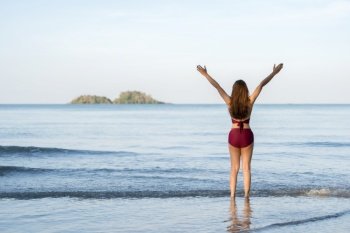 happy young woman in swimsuit with arms raised on the sea beach at Koh Chang island, Thailand