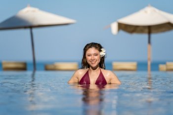 young woman in swimsuit relaxing in swimming pool with sea background