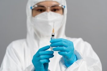 doctor in protective PPE suit holding syringe with Coronavirus (Covid-19) vaccine for injection test