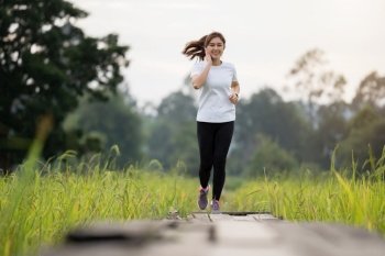 young woman listening music on earphones while running on wooden path in field