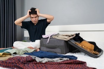 stressed man having problem with packing clothes into suitcase on bed at home, holiday travel concept