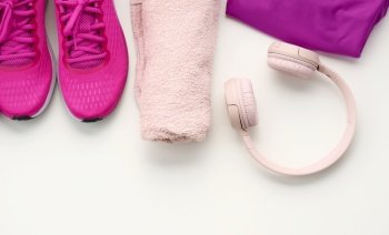 pair of textile purple sports sneakers, wireless headphones, a towel and a bottle of water on a white background. Sportswear