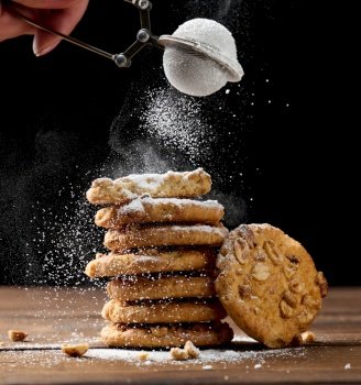 a stack of baked round cookies sprinkled with powdered sugar on a wooden table, black background