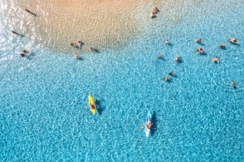 Aerial view of kayaks, swimming people in blue sea and sandy beach at sunset. Summer in Sardinia, Italy. Top view from drone of canoes, shore, transparent water. Colorful tropical landscape. Travel