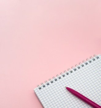 A blank checkered sheet of paper. Notepad and pen on pink. Pink Pen. Notepad spring Spiral spiral checked sheets. Vertically.. Notepad and pen on pink. Pink Pen. A blank checkered sheet of paper. Notepad spring Spiral spiral checked sheets.