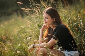 The beauty sits in the summer among the grass in the meadow.. Summer photo of a girl on the background of a grass meadow 3658.